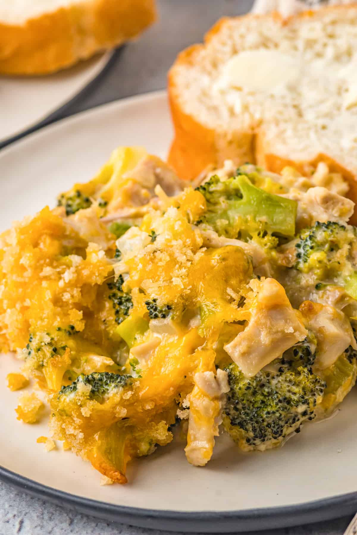 Creamy chicken and broccoli casserole on a white plate with piece of bread.