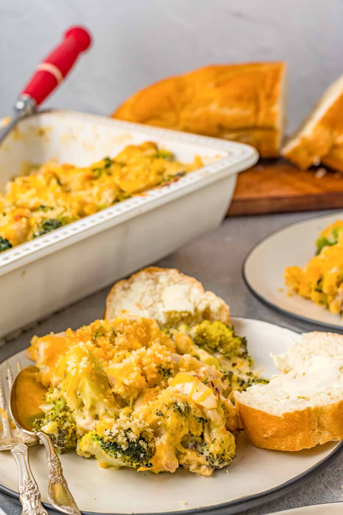 Chicken Divan Casserole  served with bread, with additional casserole and bread behind it.