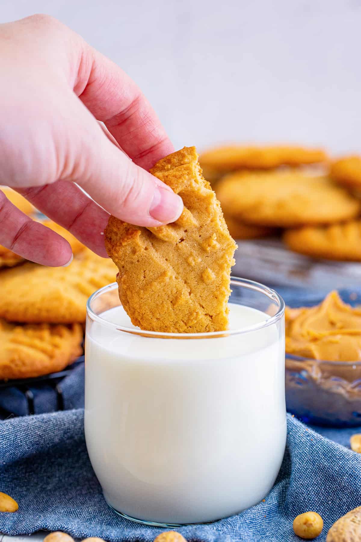 Hand dipping piece of peanut butter cookie in glass of milk.