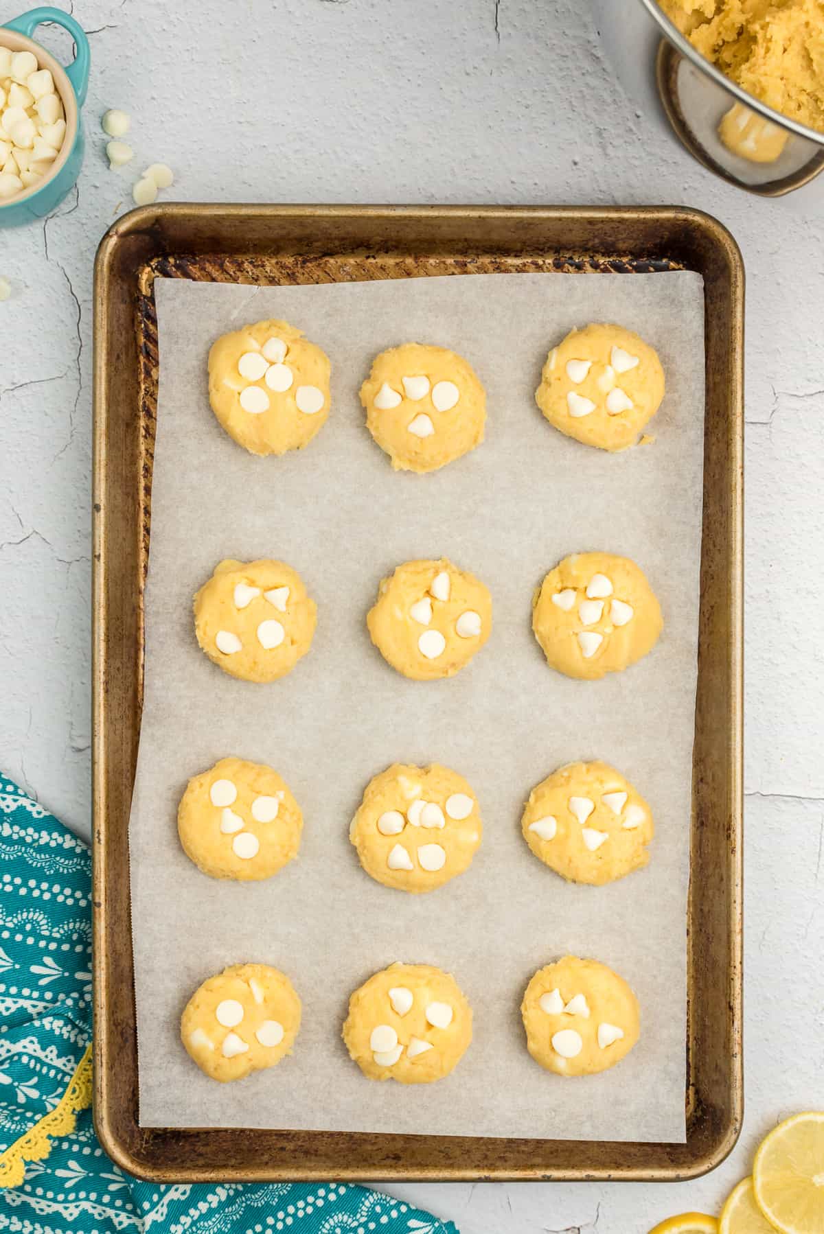 Lemon pudding mix cookie dough with white chocolate chips on lined baking sheet.