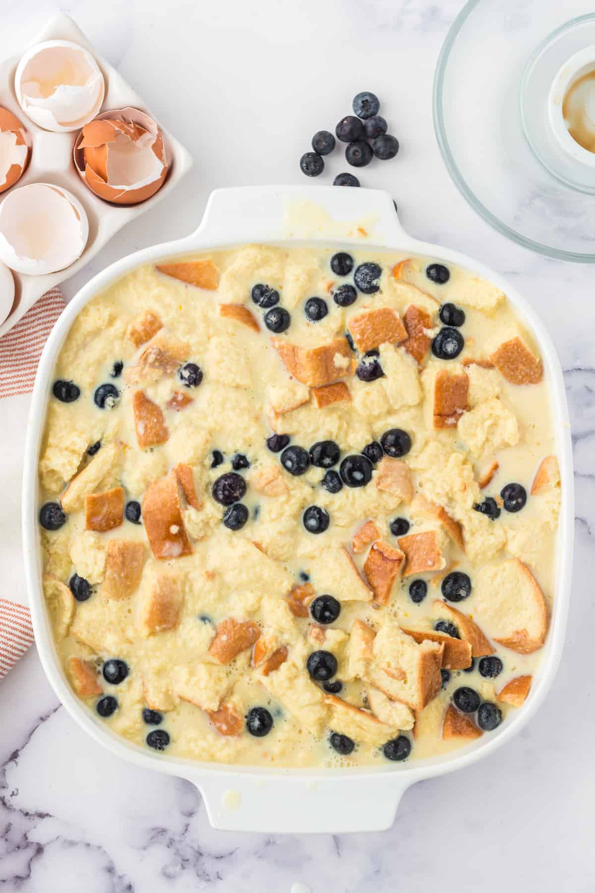 Unbaked lemon blueberry bread pudding in square casserole dish.
