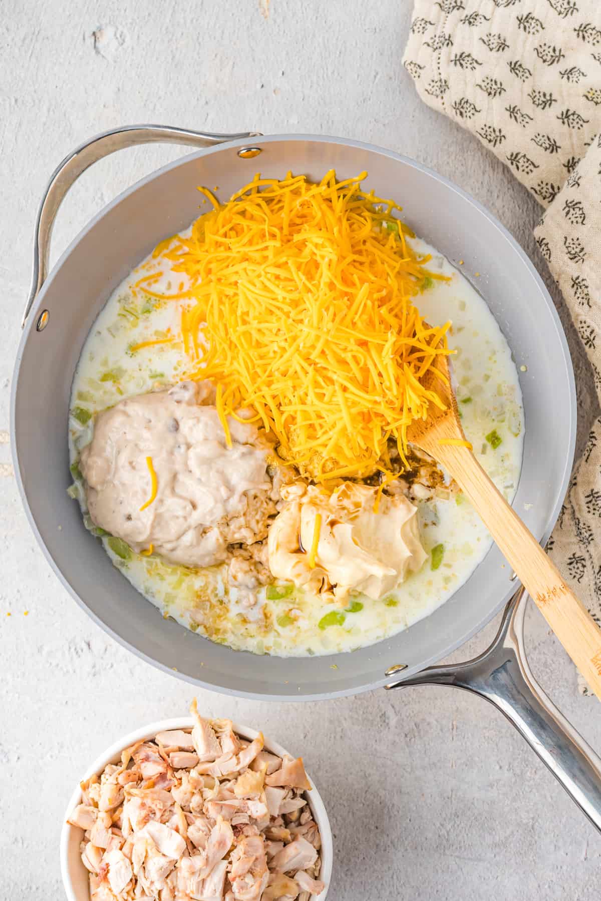 Shredded cheese, soup, mayo, sour cream, and other ingredients added to pan.