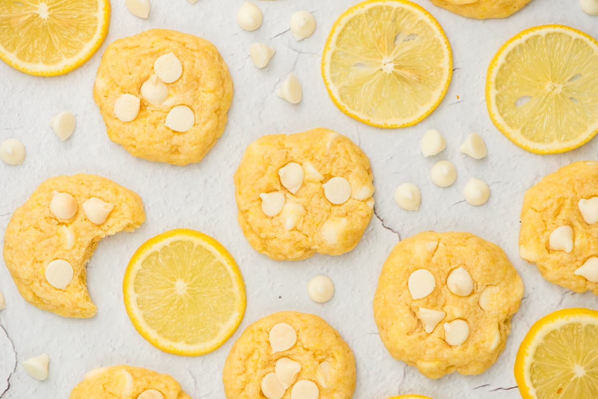 Soft lemon cookies on table with white chocolate chips and lemon slices.