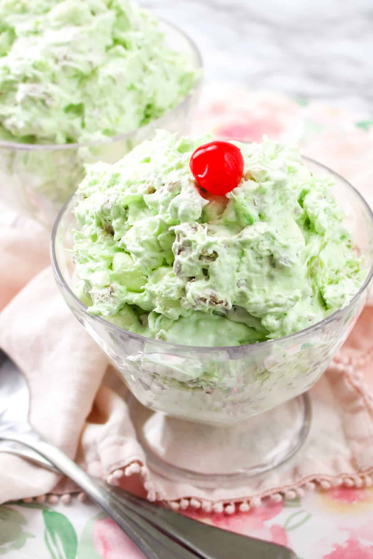 Watergate salad in serving glass and topped with cherry.
