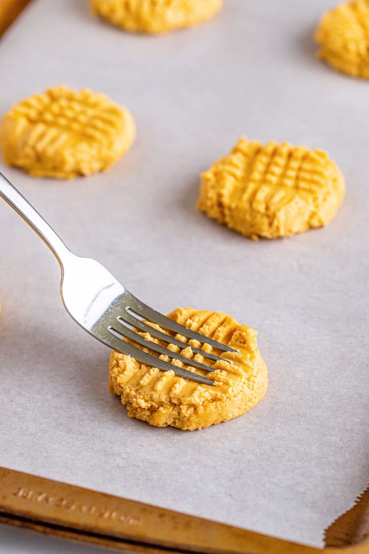 Fork pressing down on peanut butter cookie dough to create criss cross pattern.