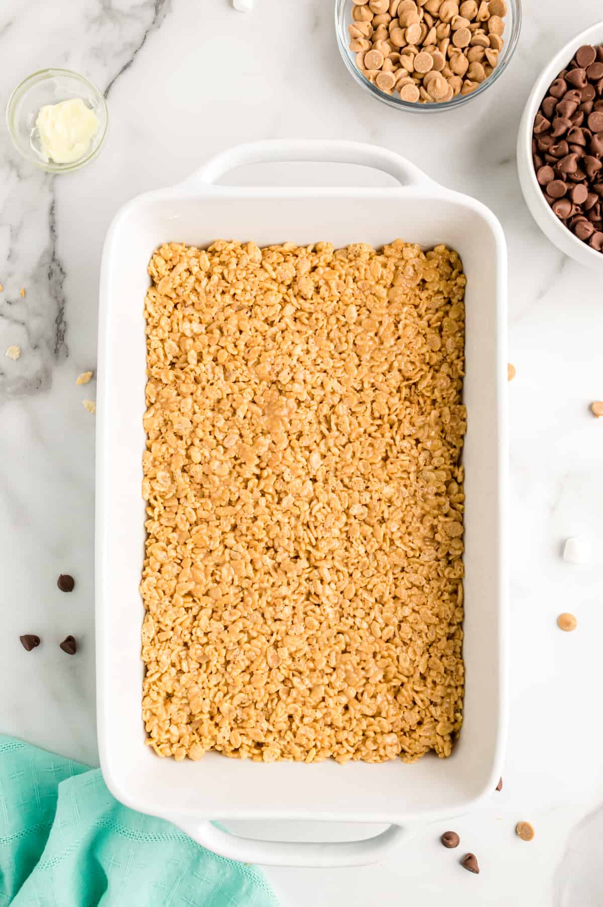 Peanut butter rice cereal mixture pressed into white 9 by 13 inch baking pan.
