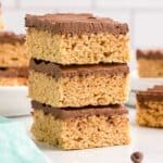 Peanut butter rice krispie treats with chocolate topping stacked on top of each other on white plate.