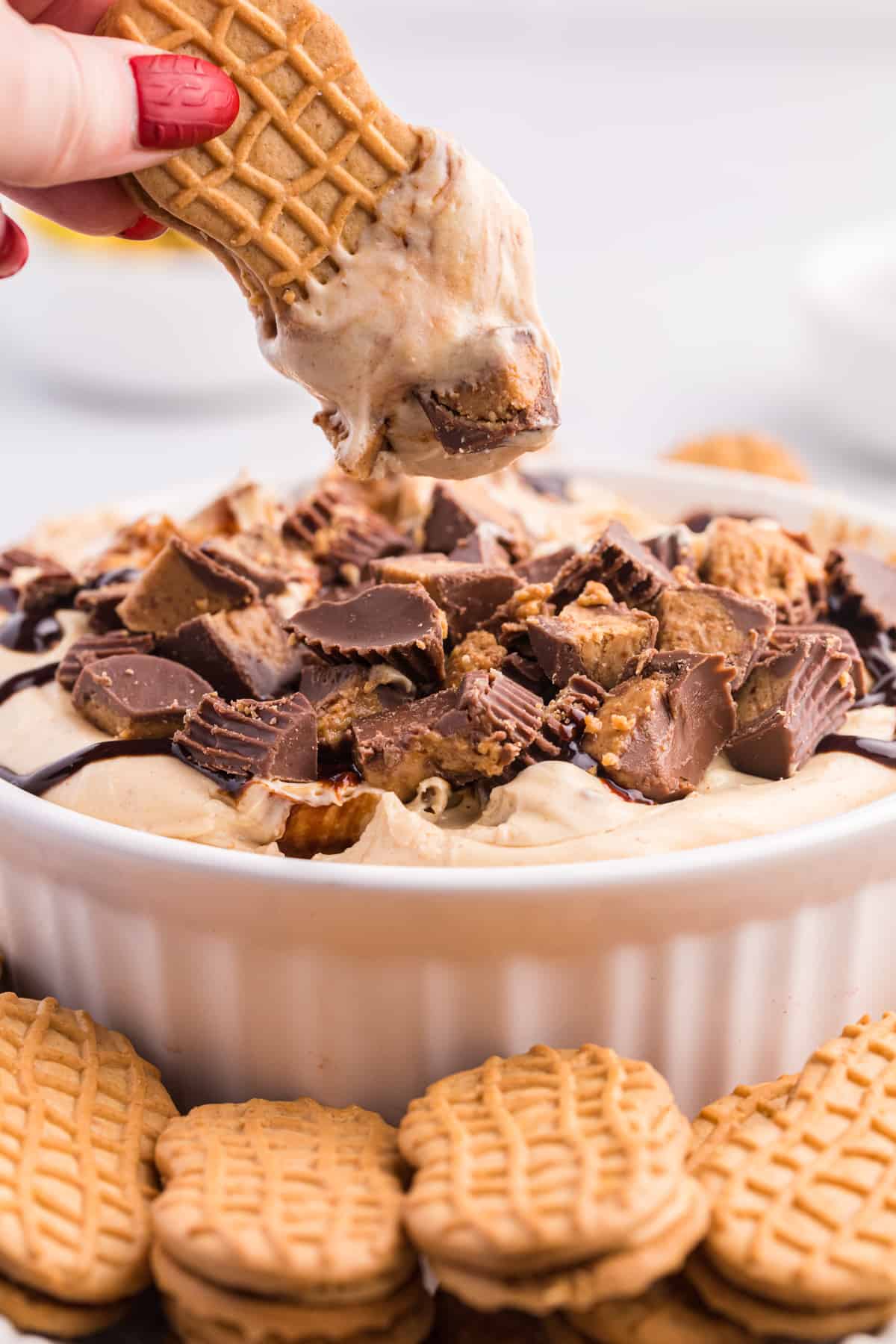 Hand reaching in and dipping Nutter Butter cookie in peanut butter cheesecake dessert dip.