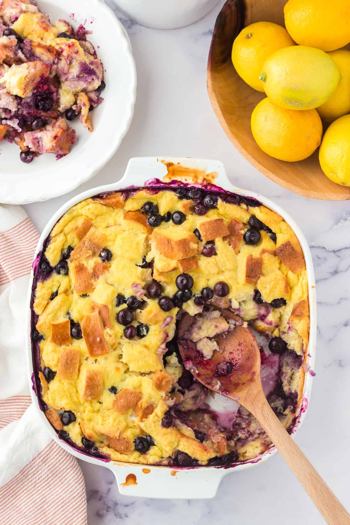 Lemon Blueberry Bread pudding with wooden serving spoon resting in dish after several servings were removed.