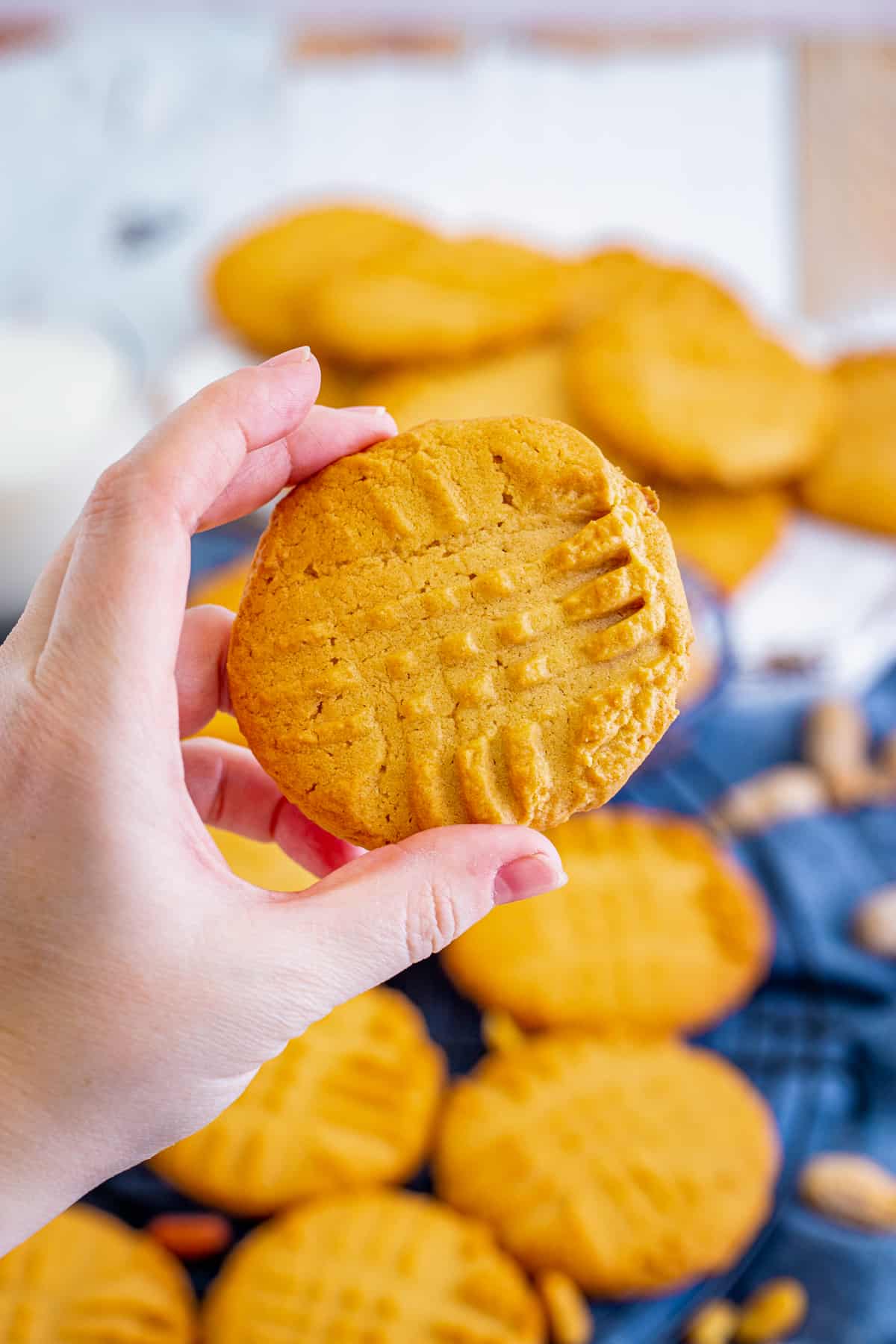 Hand holding a large, crispy peanut butter cookie with fork marks on top.