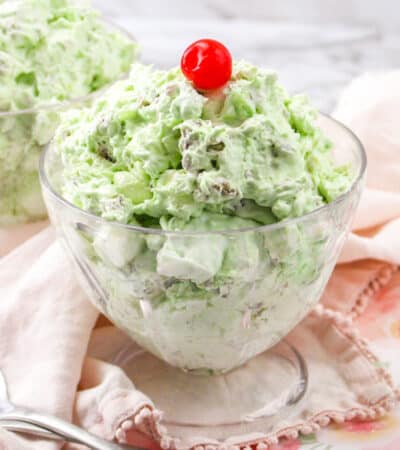 Watergate salad in a glass bowl topped with cherry.