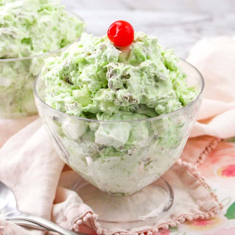 Watergate salad in a glass bowl topped with cherry.