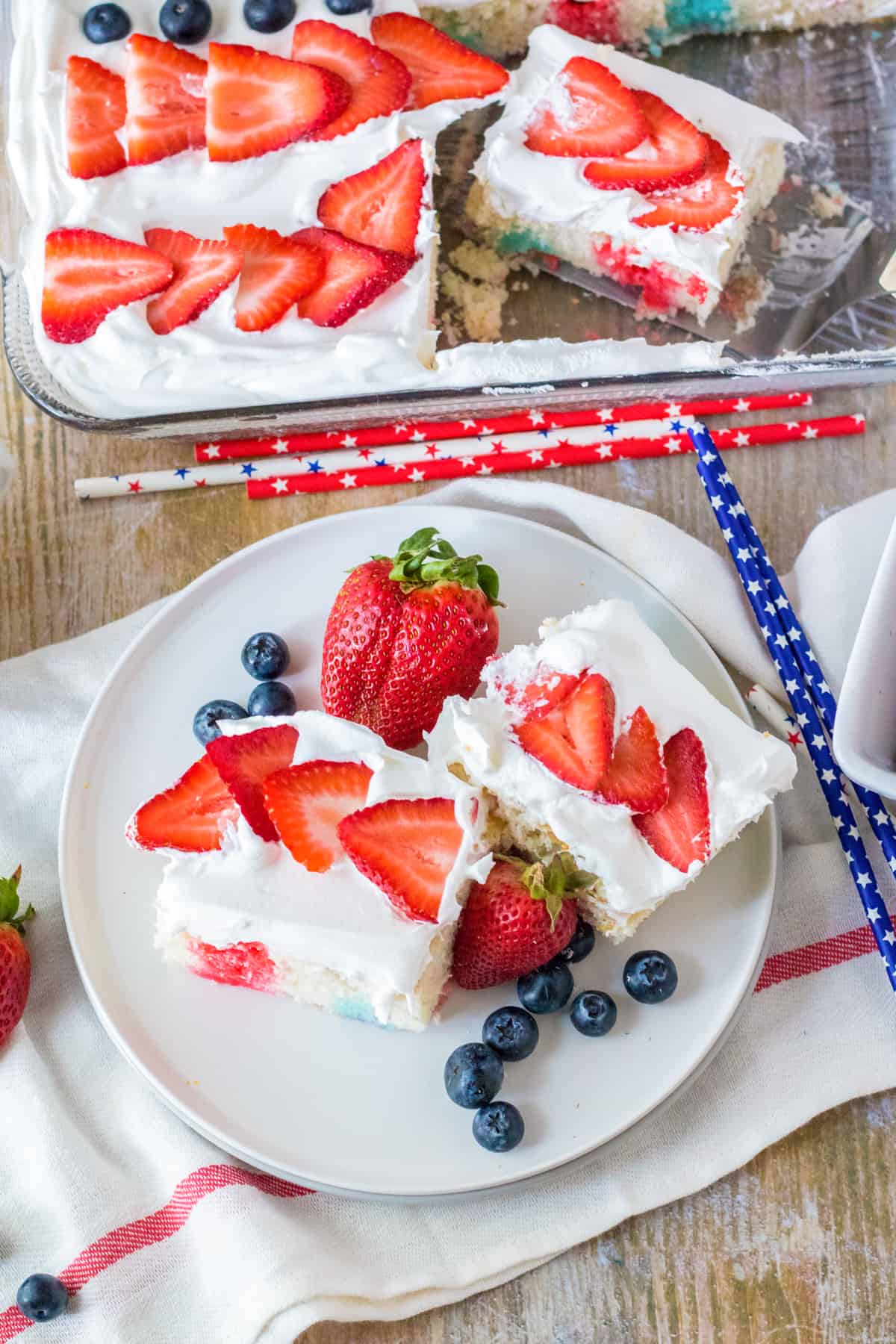 4th of July flag cake topped with fresh fruit. Two slices are removed and placed on plate with fresh berries.