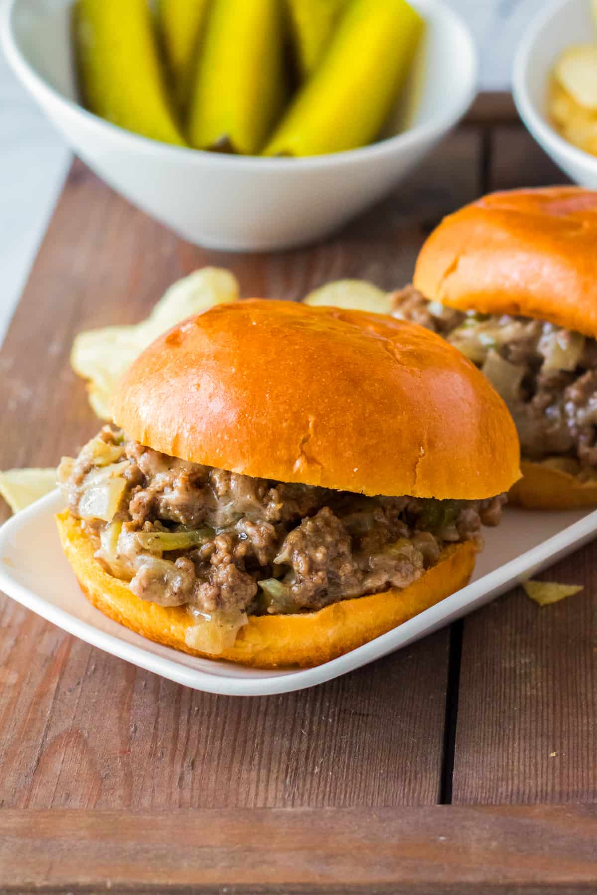 Sloppy joes with cheese, peppers, and onions on soft buns served with pickles and chips.