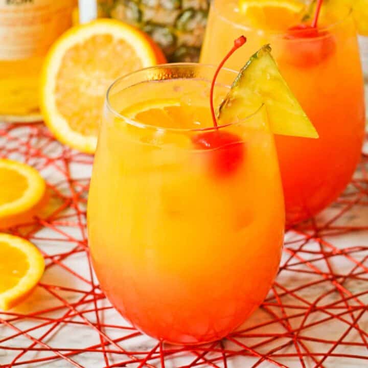 Yellow, orange, and red cocktail with cherry, pineapple, and oranges.