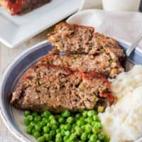 Copycat cracker barrel meatloaf sliced on plate served with peas and mashed potatoes.