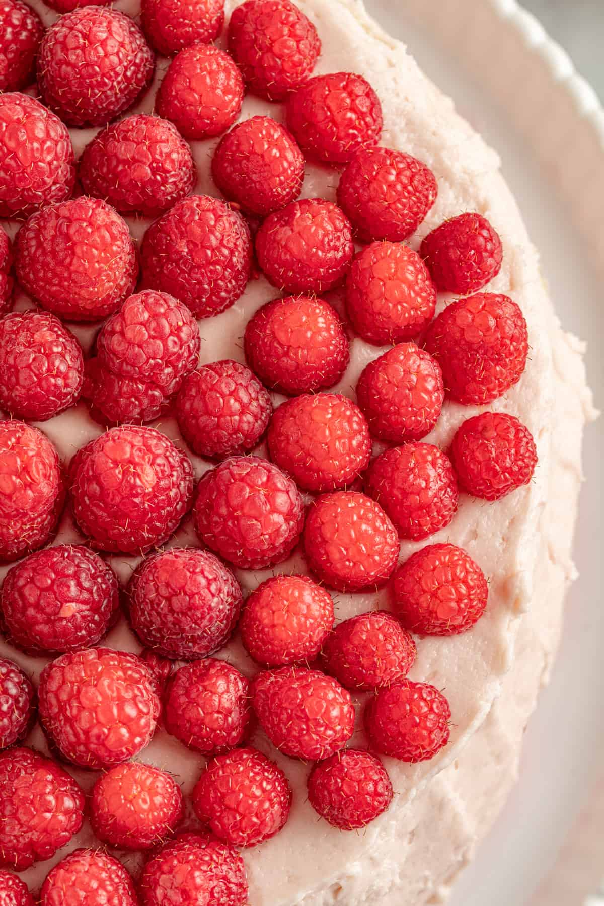 Round cake topped with pink frosting and fresh raspberries.
