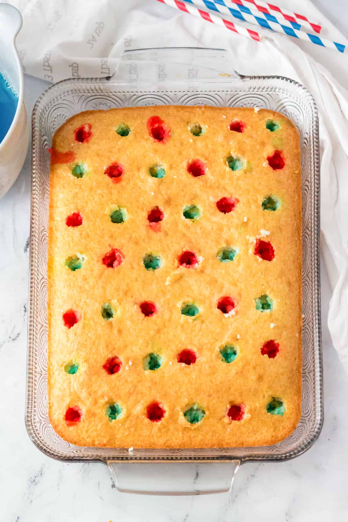 Golden cake with holes poked throughout the top and red and blue jello poured into alternating holes.