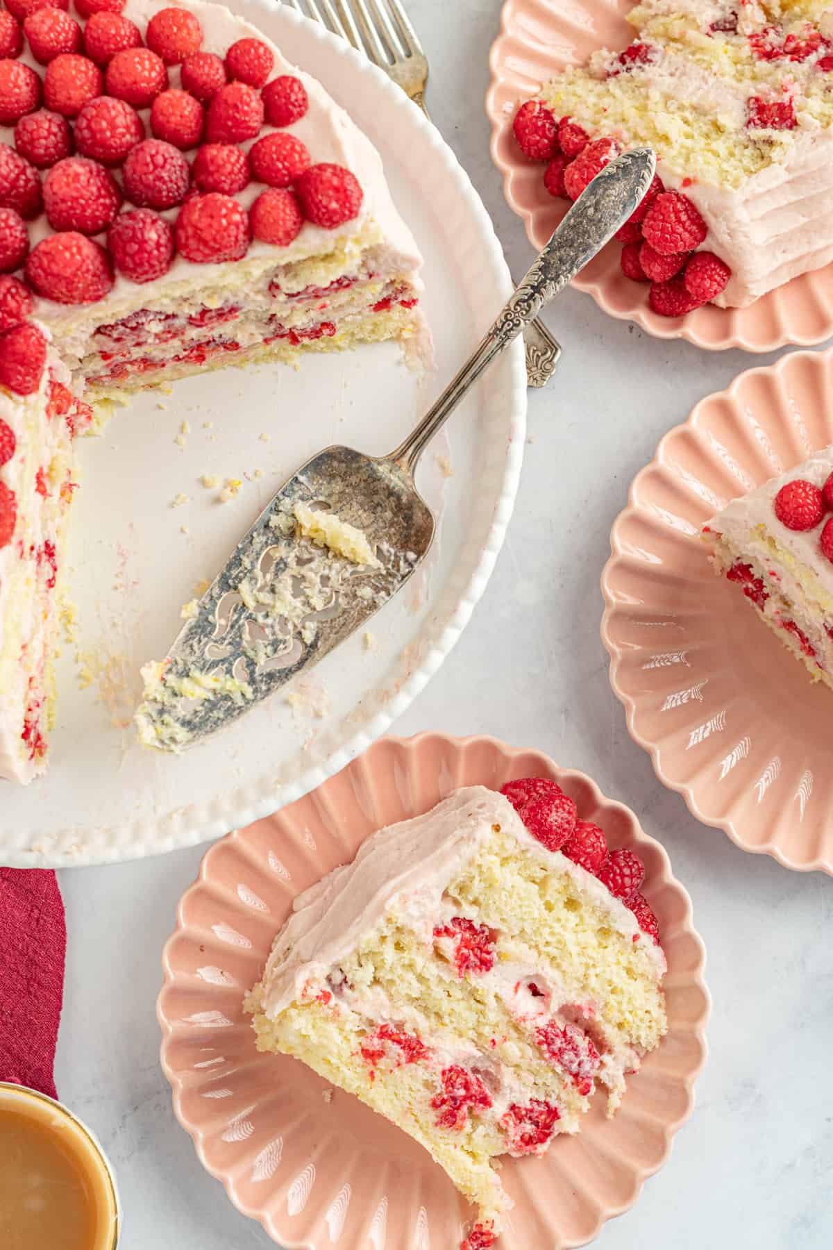 Slices of raspberry lemon cake on plates next to remaining layer cake.