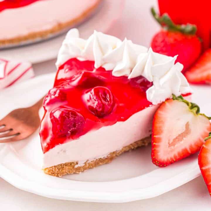 Slice of no bake strawberry cheesecake with strawberry topping and whipped cream piping on edge.
