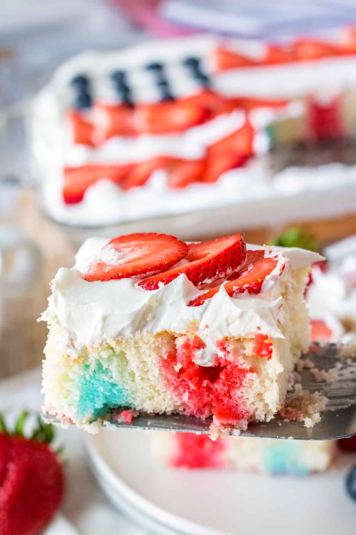 A piece of patriotic poke cake being lifted out of the cake to be served.