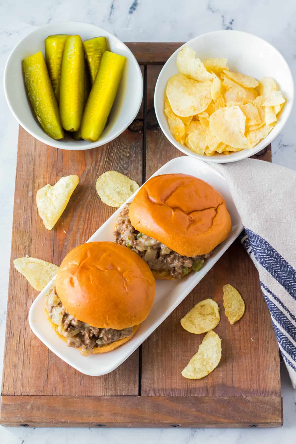Slow cooker sloppy joes served on buns with potato chips and pickle spears.