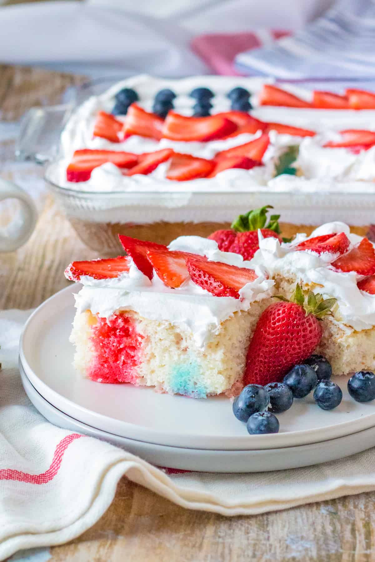 4th of July poke cake with red and blue jello, cool whip topping, and fresh berries in the shape of a flag on top.