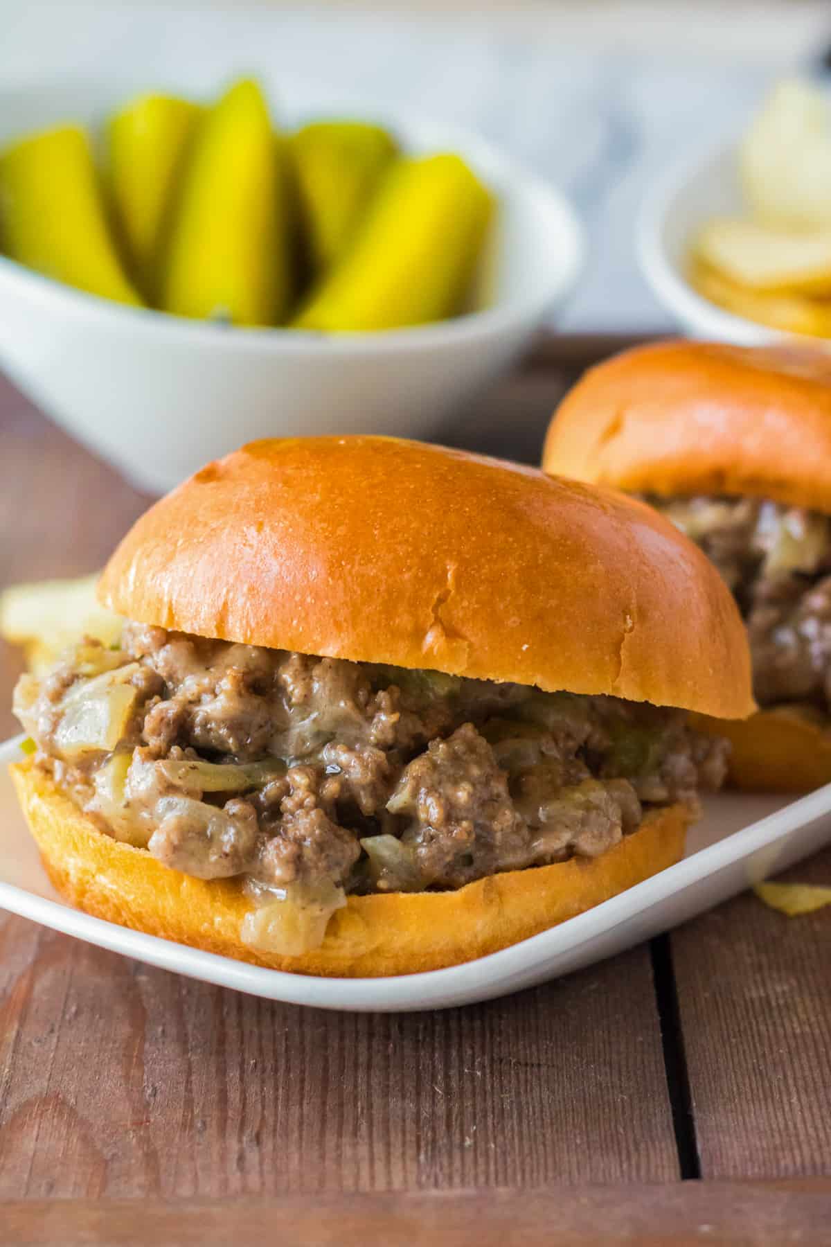Slow Cooker Philly Cheesesteak Sloppy Joes on brioche buns with pickles in the background.