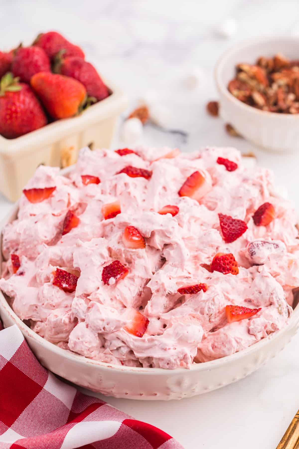 Strawberry Fluff Dessert Salad with fresh strawberries and pecans in the background.