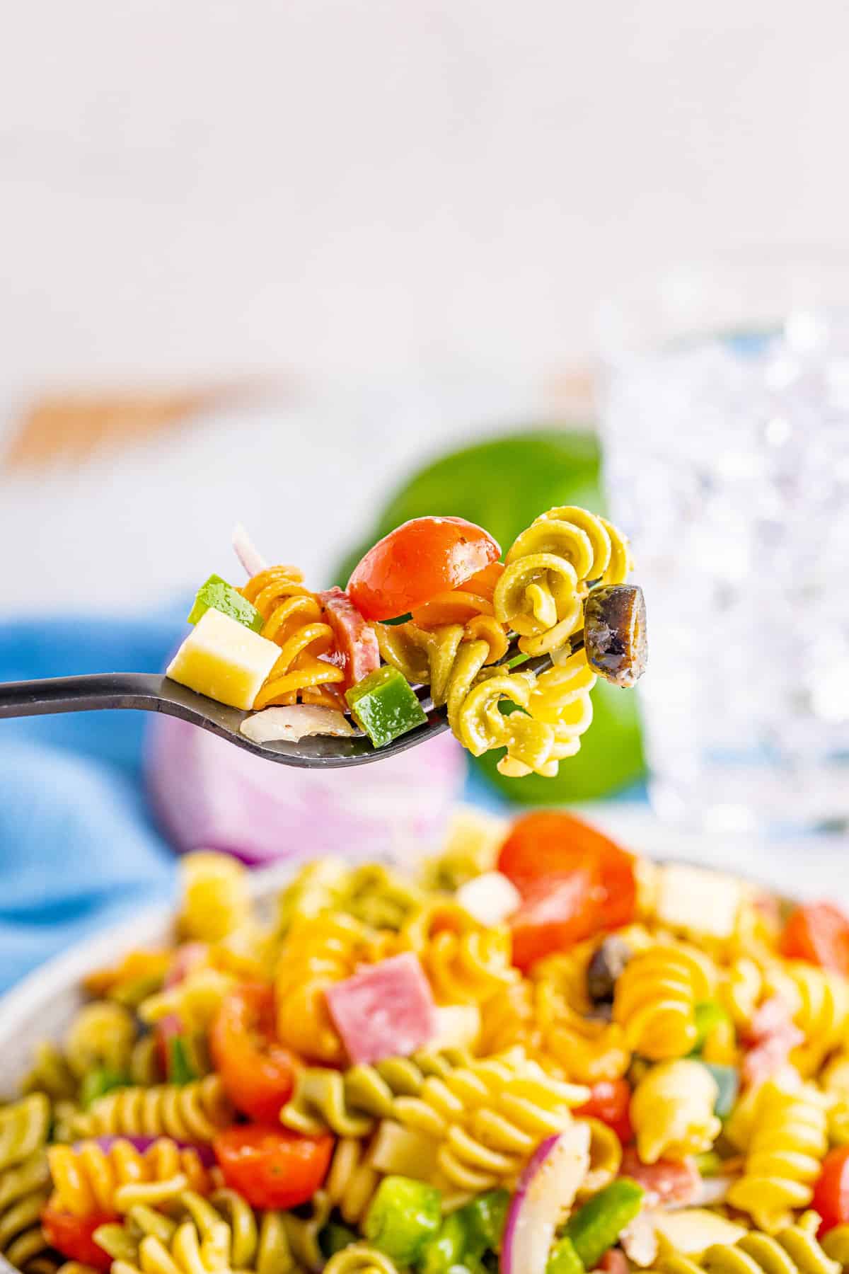 Fork with bite of pasta salad containing rotini, grape tomato, diced green pepper, and mozzarella cheese.
