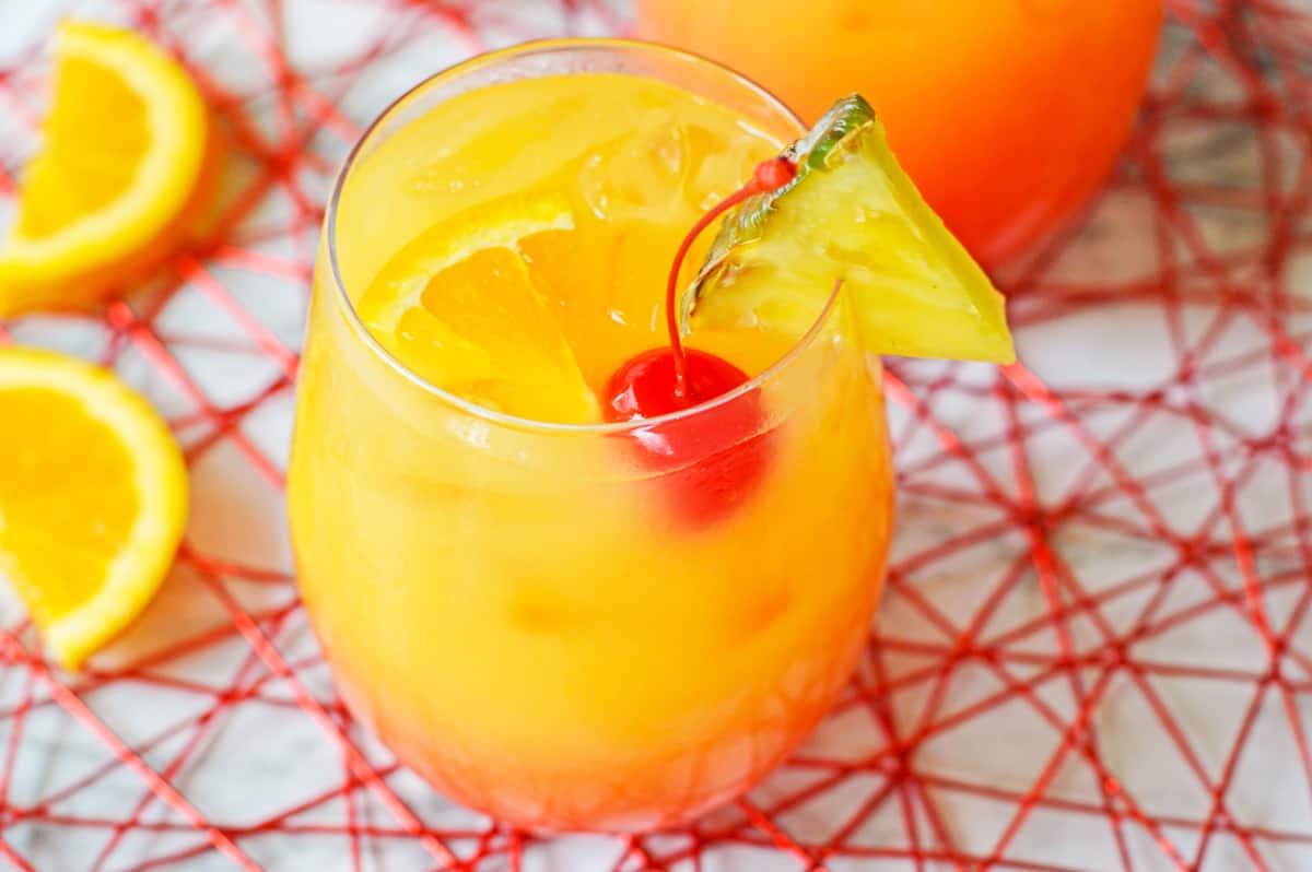 Yellow, orange, and red ombre cocktail garnished with cherry , orange, and pineapple.
