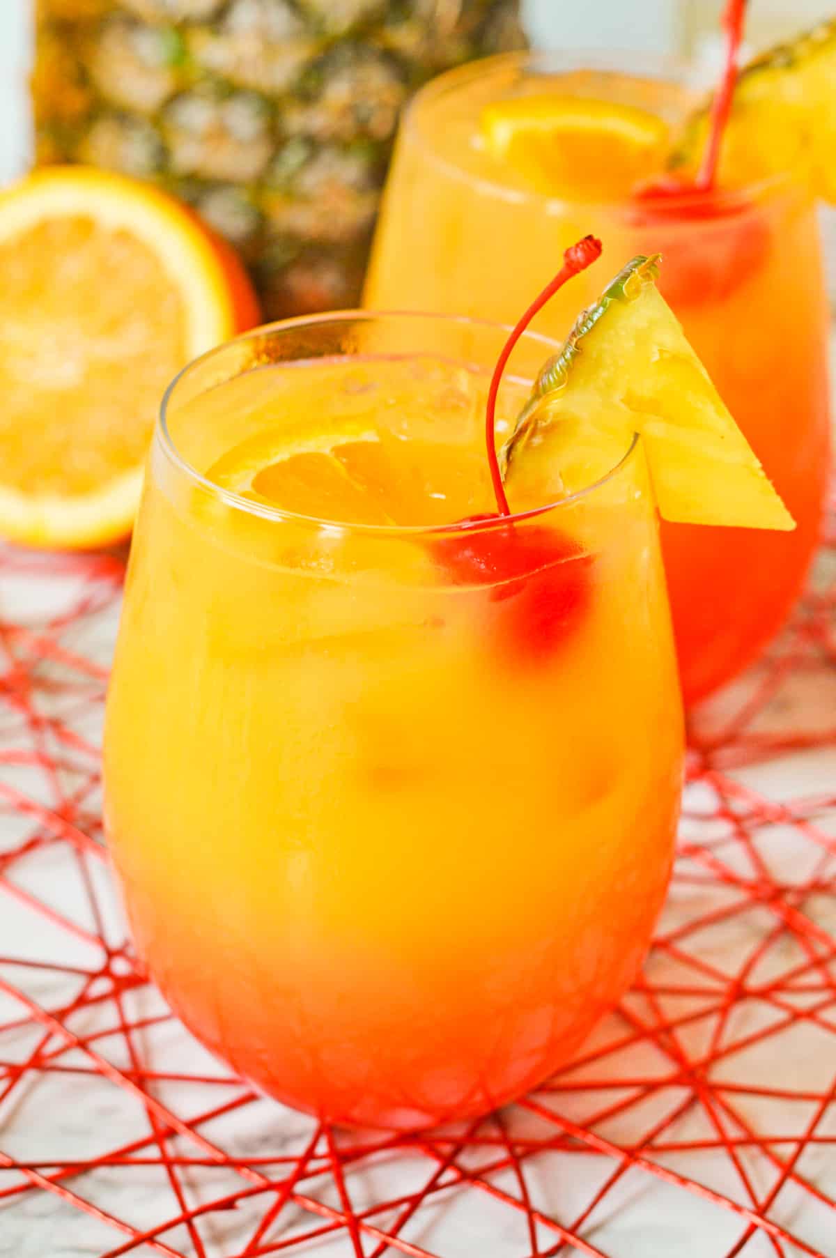 Ombre Caribbean rum punch in a cocktail glass garnished with pineapple and cherry.