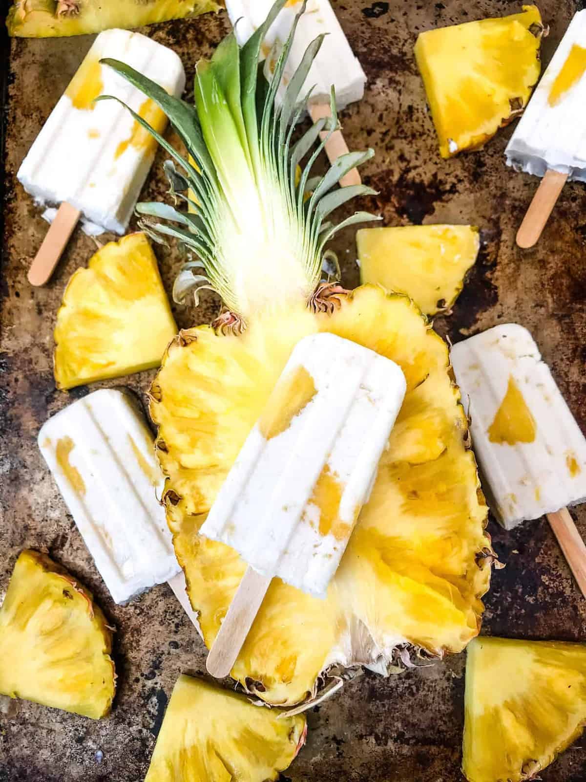 Pine colada popsicles on tray with pineapple.