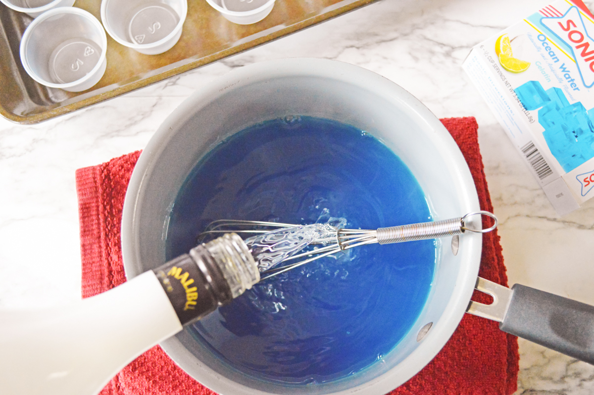Bottle of Malibu coconut rum being poured into blue jello mixture to make shark shots.