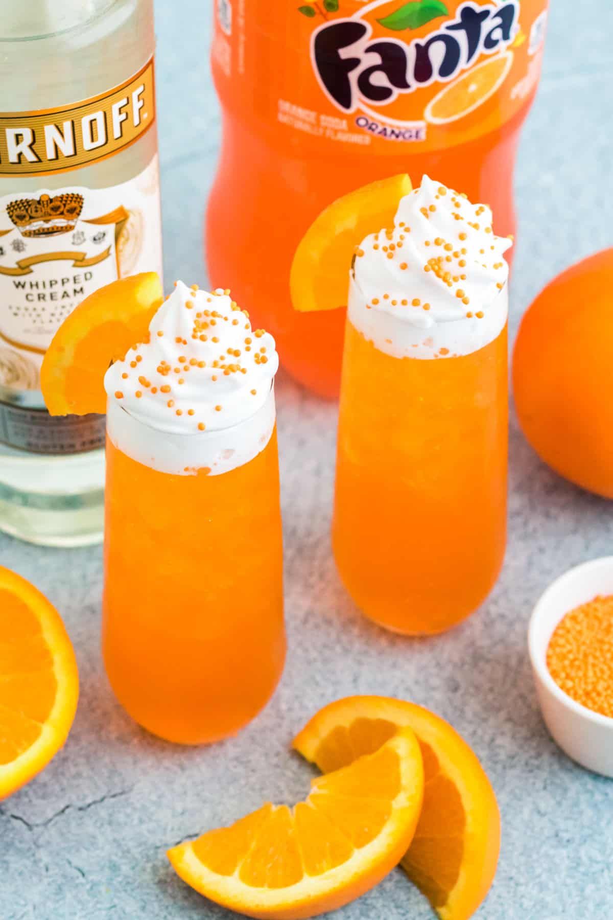 Two creamsicle cocktail drinks next to vodka, orange soda, and fresh orange wedges.