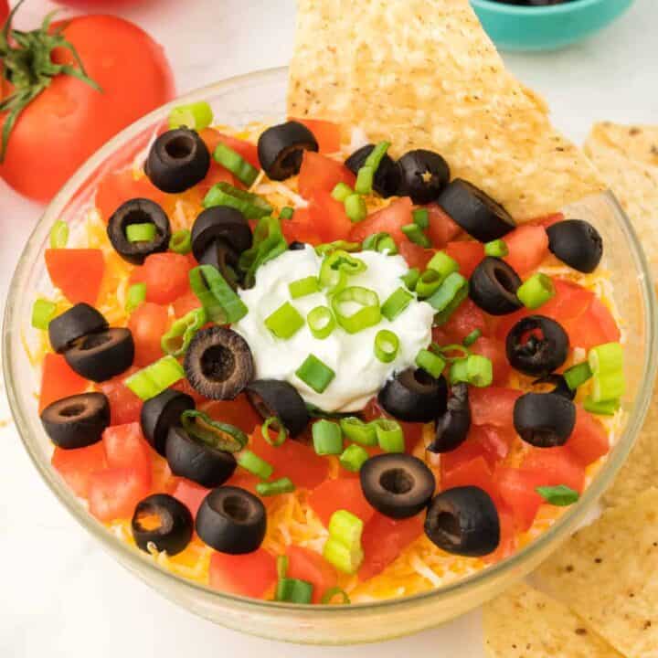 Layered taco dip with tortilla chips for dipping.