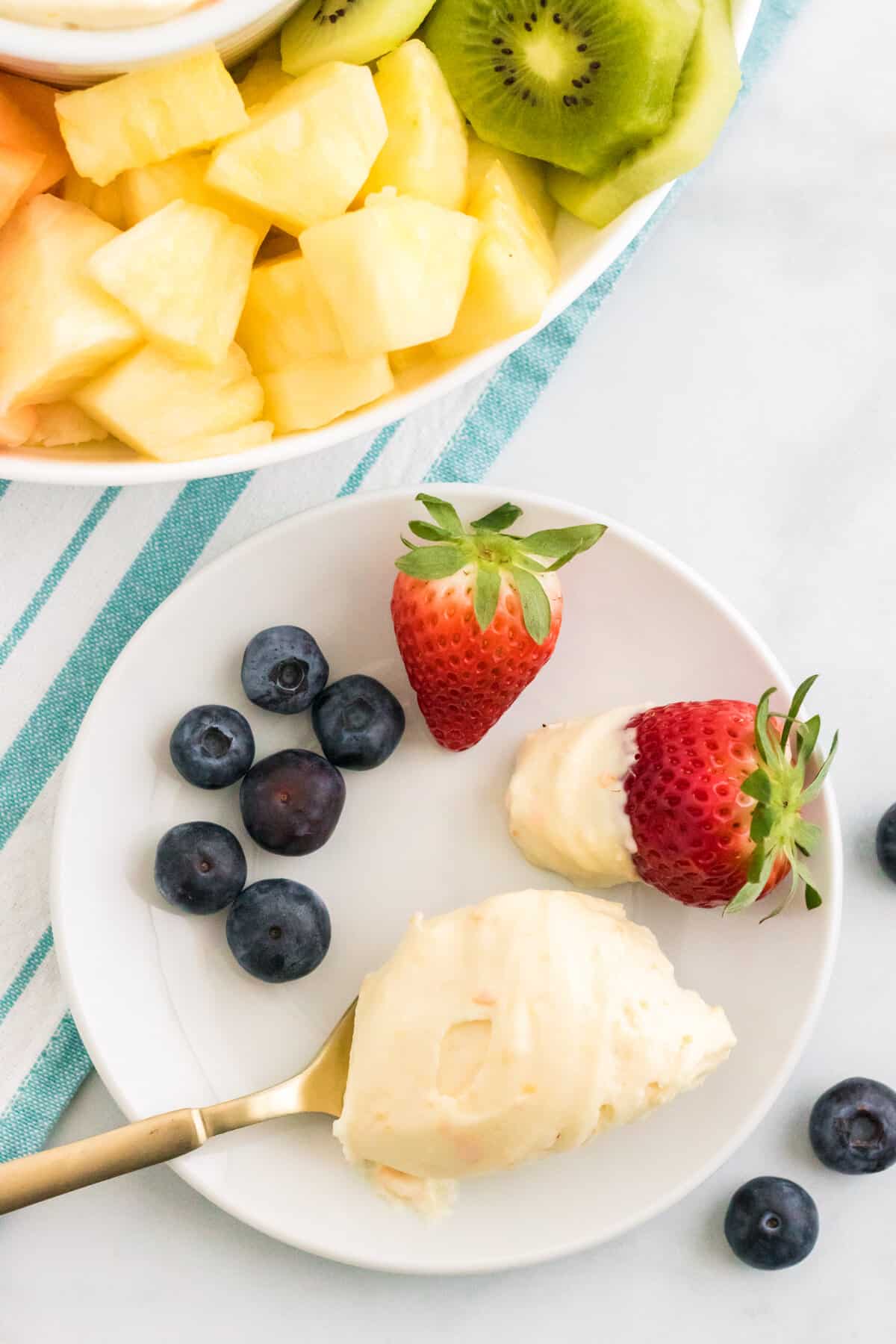 Spoonful of creamsicle fruit dip on a white plate with fresh fruit.