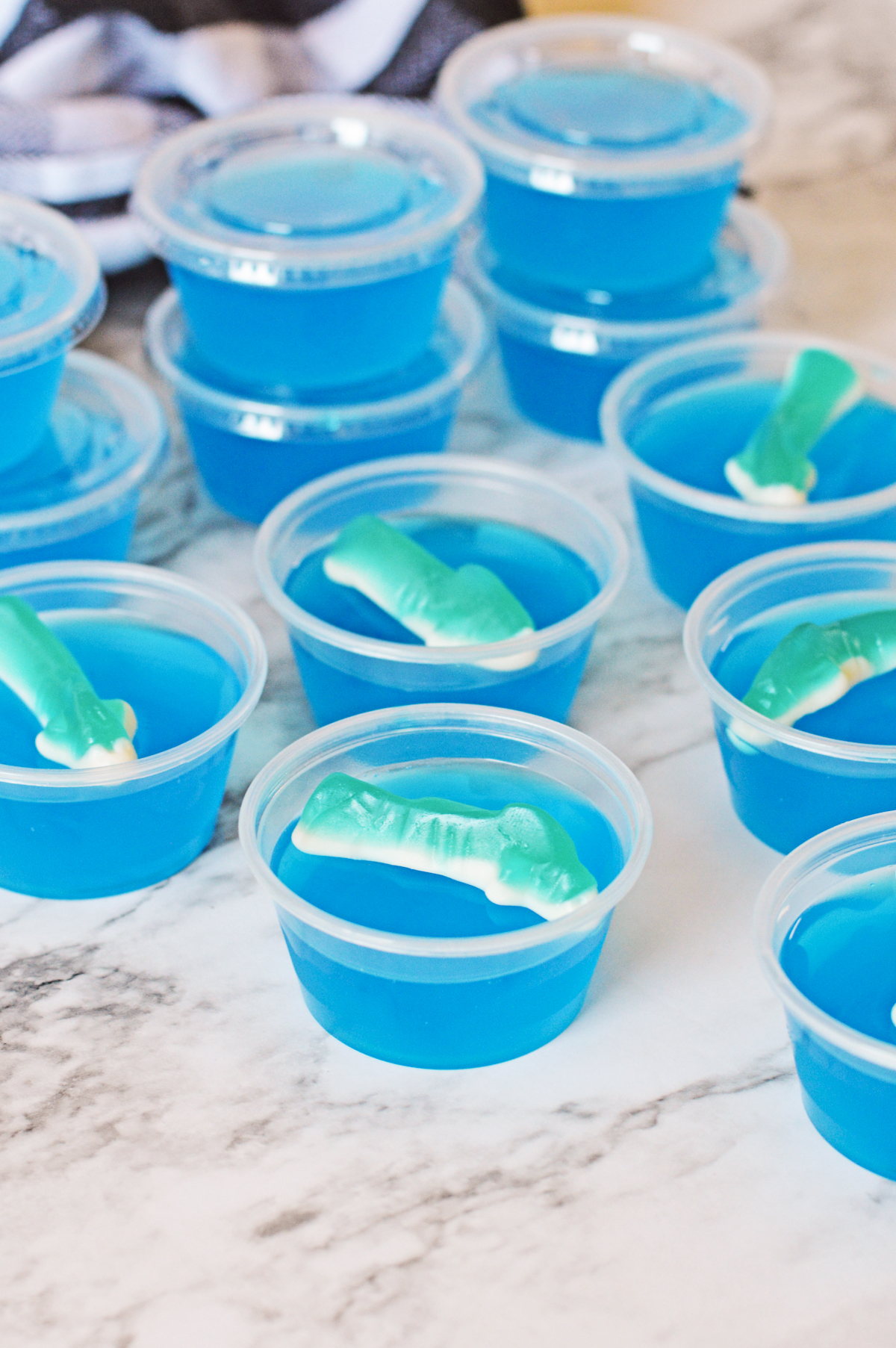 Shark bite jello shots topped with shark gummies, some with lids on the shot cups.