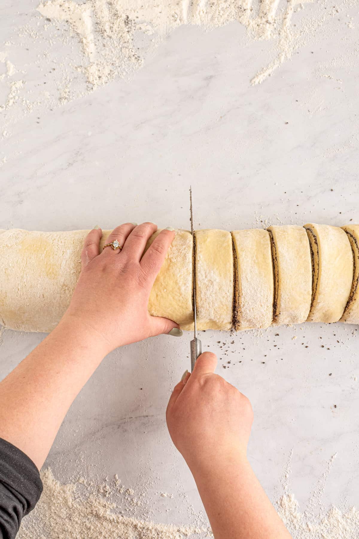 Hands slicing rolled dough into individual rolls.
