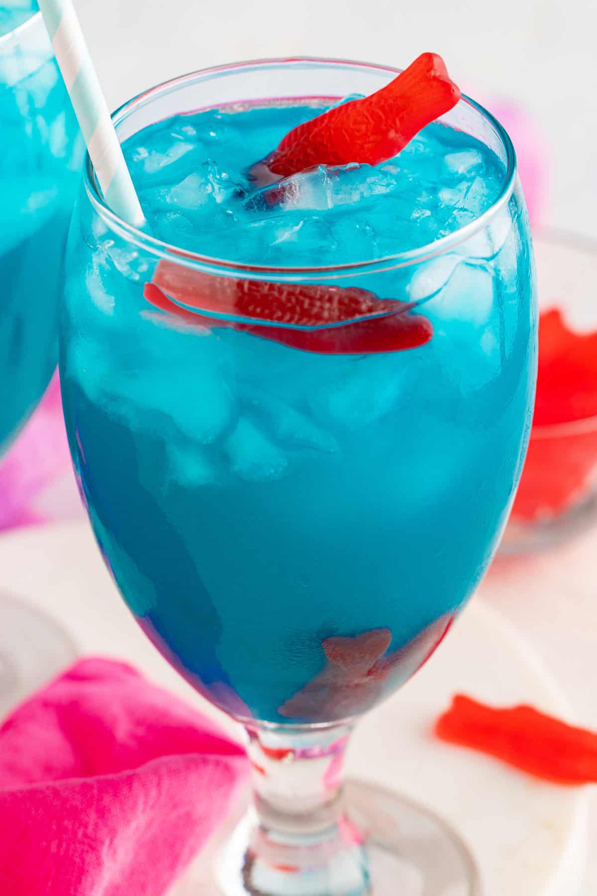 Blue ocean water cocktail in a wine glass with red candy fish sticking out of the top.
