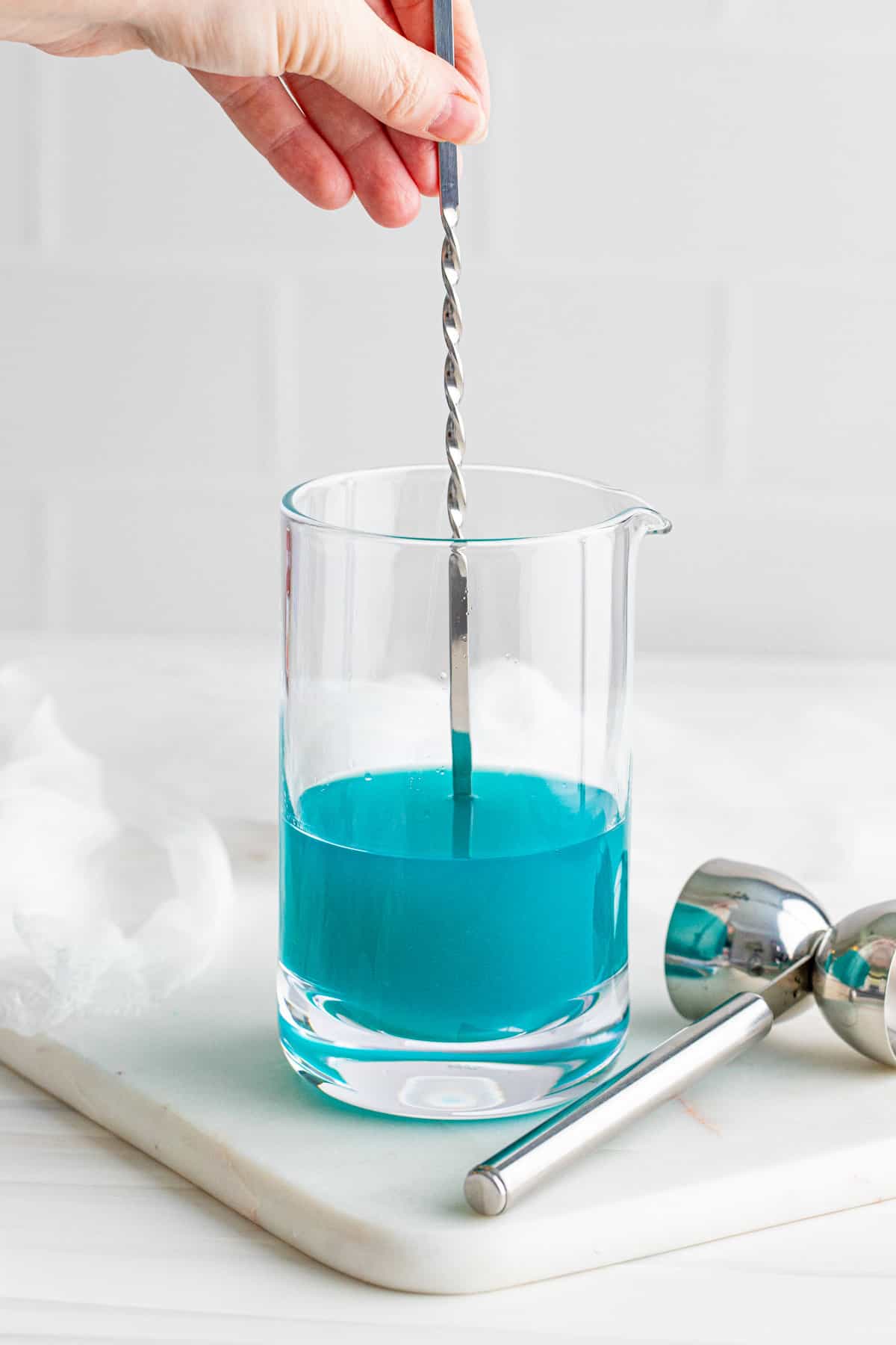 Stirring blue cocktail in large mixing glass.