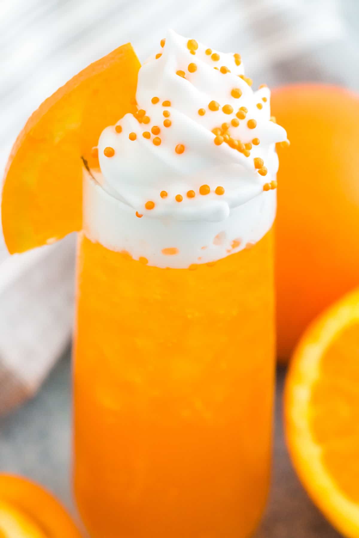 Orange creamsicle cocktail in a tall glass topped with whipped cream, orange slice, and orange sprinkles.