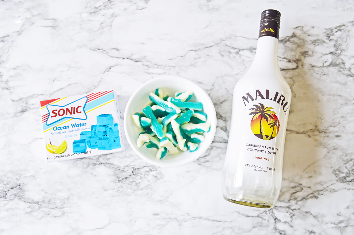 Box of sonic ocean water jello, blue shark gummy candies in a bowl, and bottle of Malibu rum.