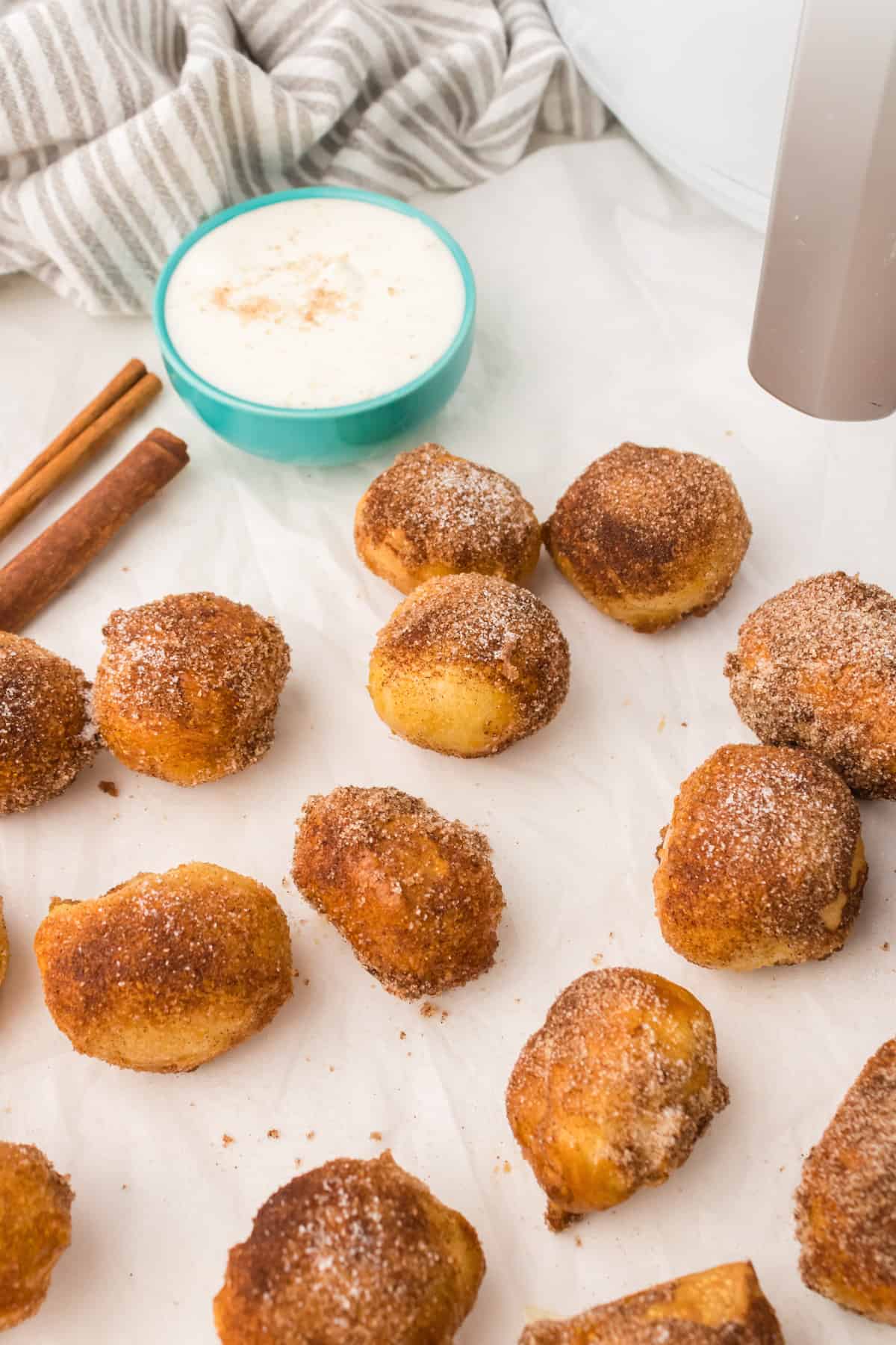 Cinnamon sugar covered pretzel bites on sheet of parchment paper with dipping sauce in the background.