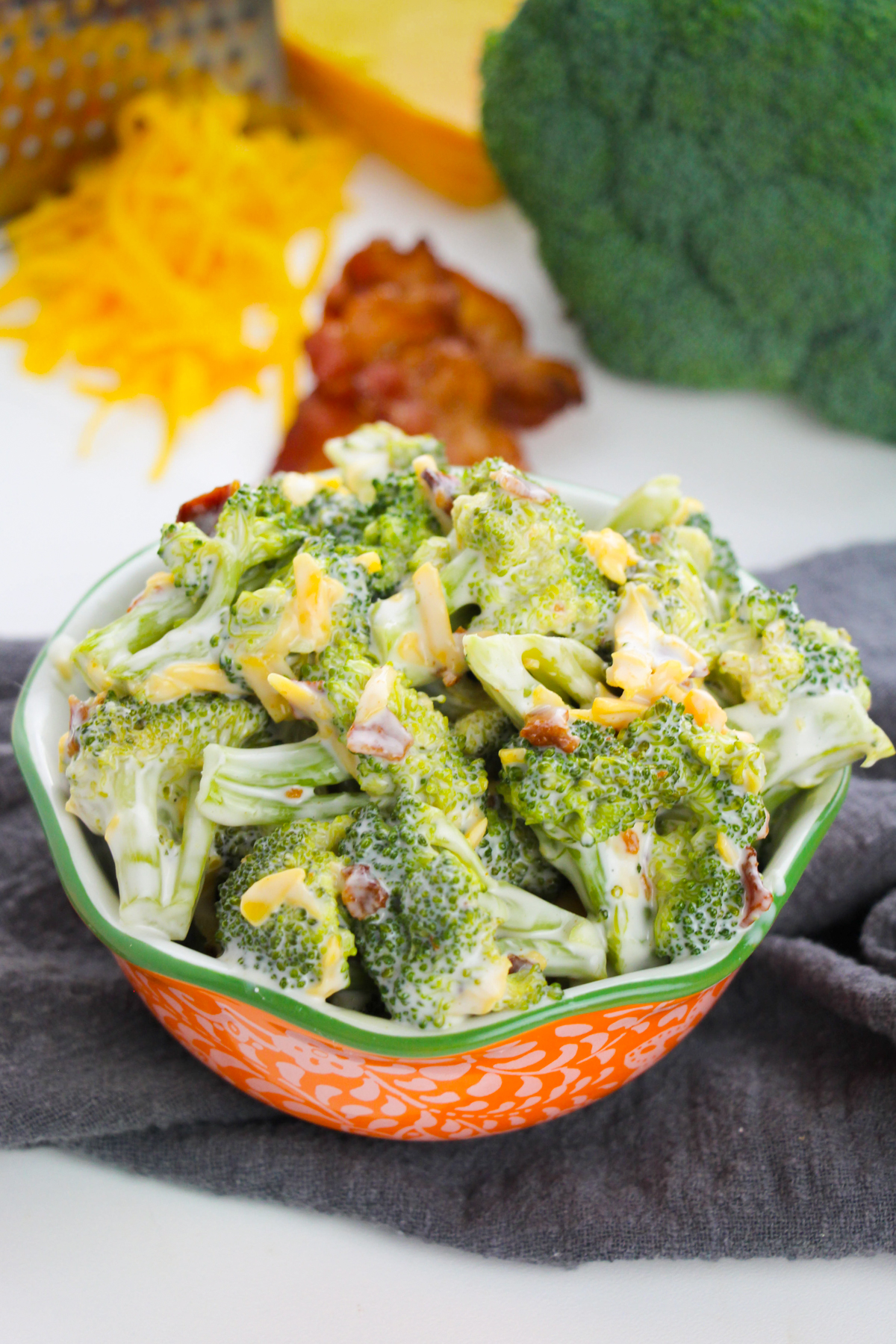 Broccoli salad with bacon and cheddar cheese in orange and green serving bowl.