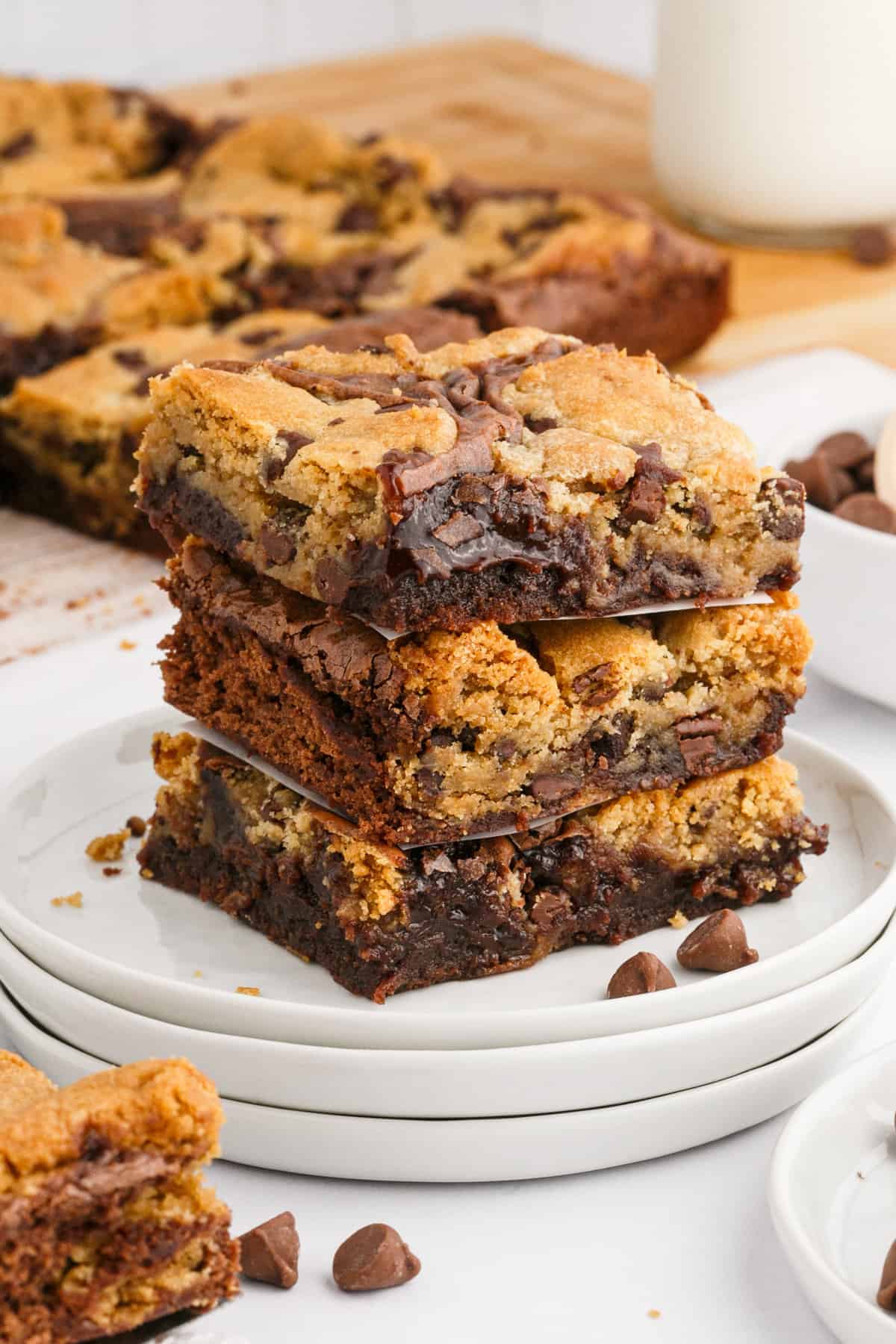 Chocolate chip brookies stacked three high on a white plate with rest of batch behind them.