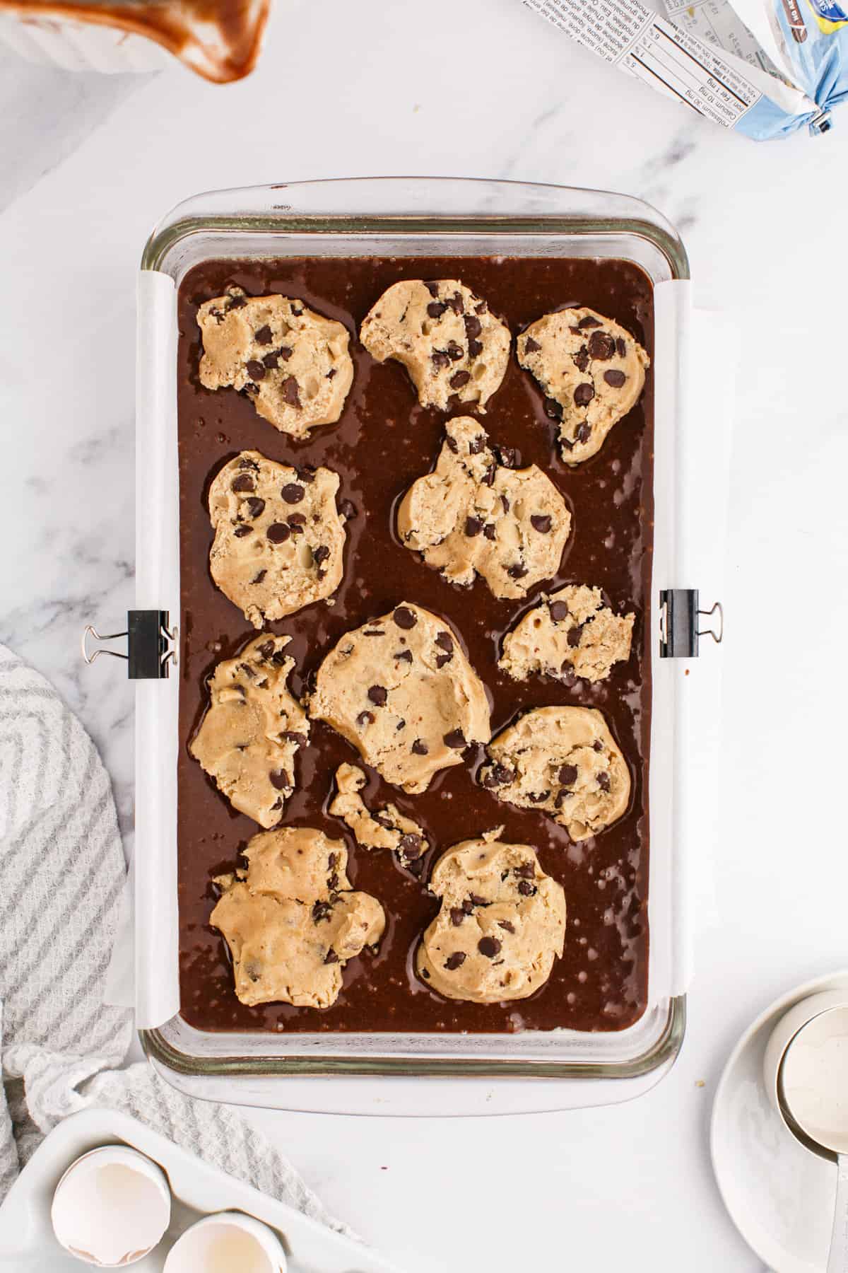 Chocolate chip cookie dough on top of brownie batter in casserole dish.