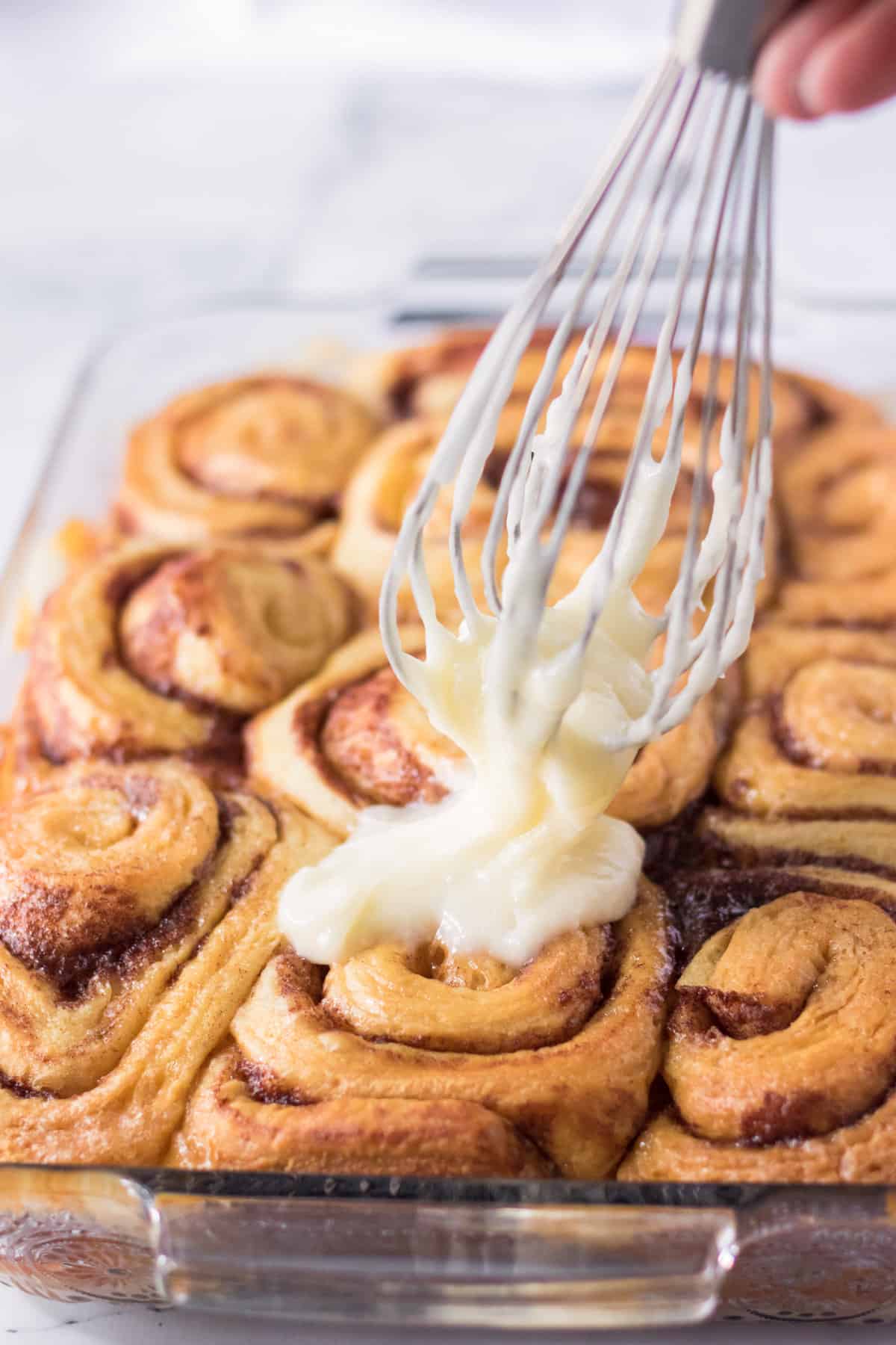 Cream cheese icing being spread on the baked cinnamon rolls.