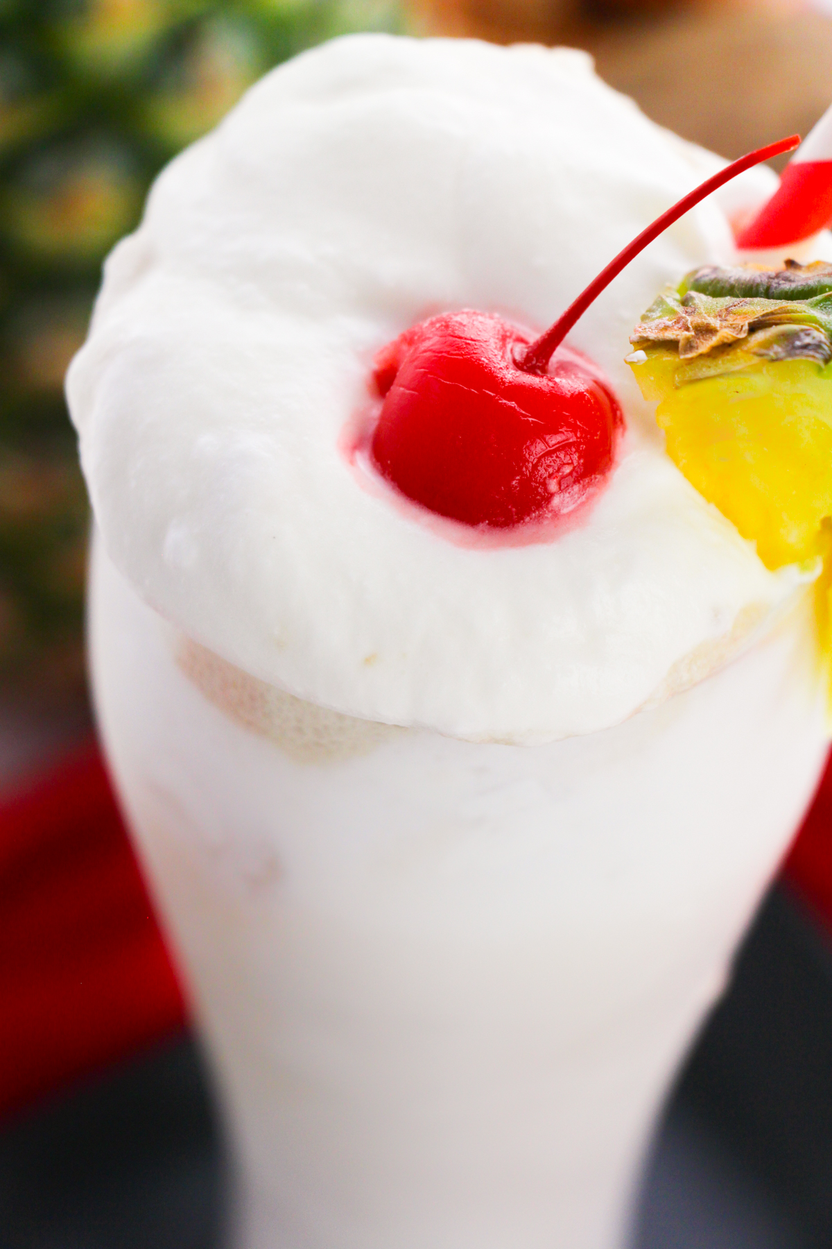 Creamy white frozen cocktail topped with whipped cream, cherry, and pineapple.