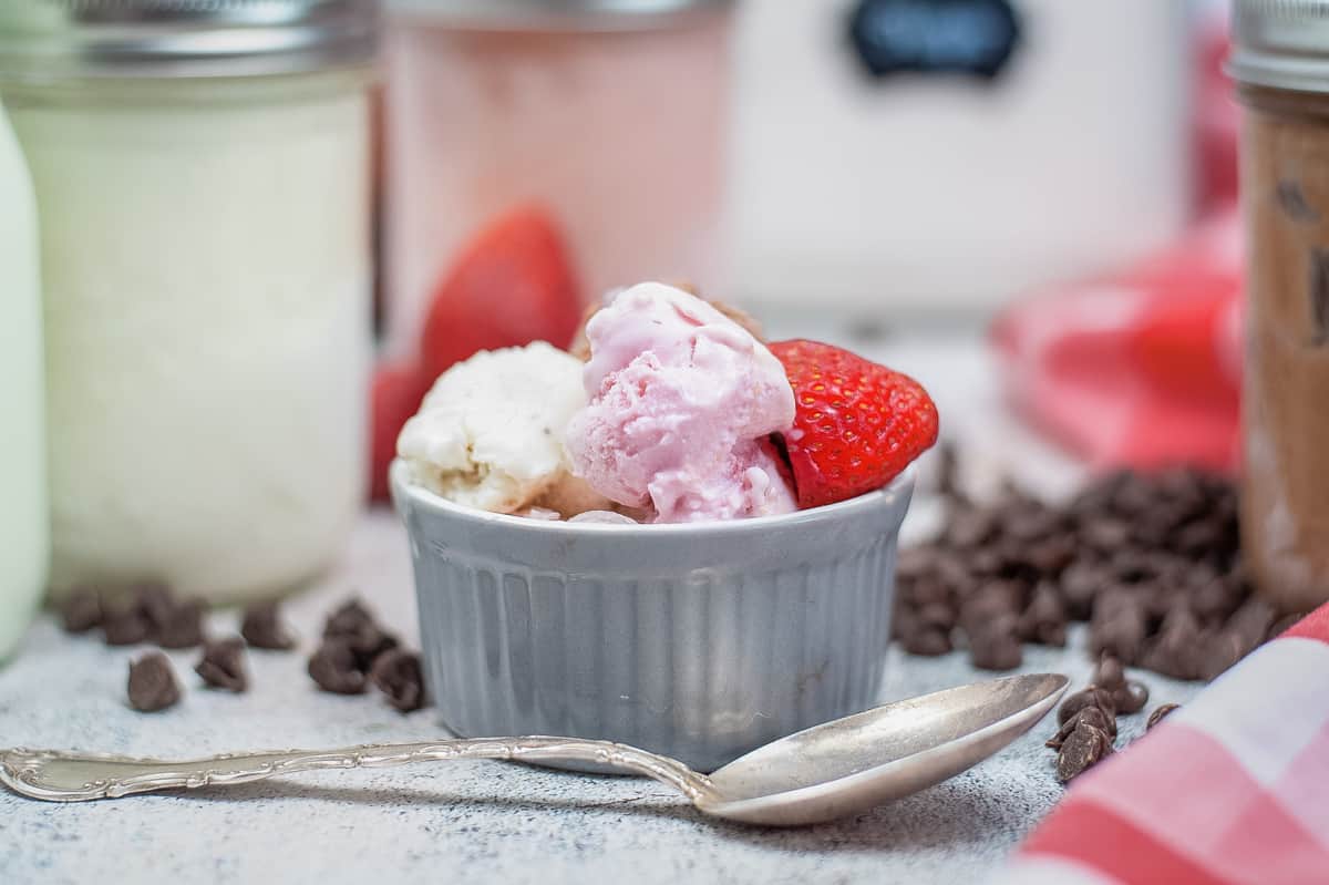 Neapolitan mason jar ice cream in bowl with spoon and jars of ice cream in the background.